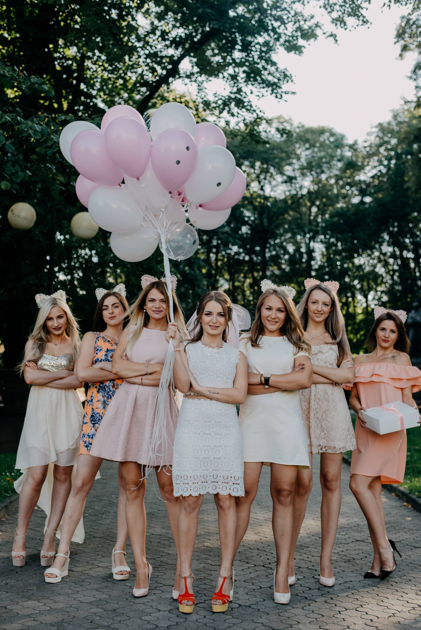 A bride surrounded by her bridesmaids and holding a bunch of pink balloons